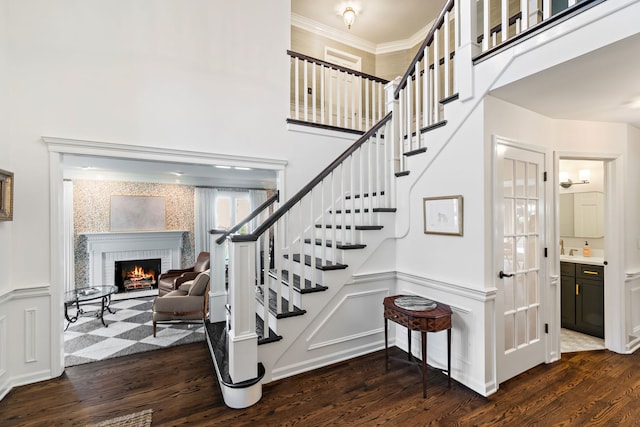 staircase featuring wood-type flooring, ornamental molding, and a fireplace