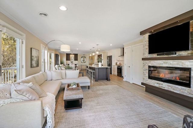 living room with a stone fireplace, light hardwood / wood-style flooring, and crown molding