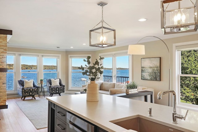 kitchen with sink, light wood-type flooring, pendant lighting, a water view, and crown molding