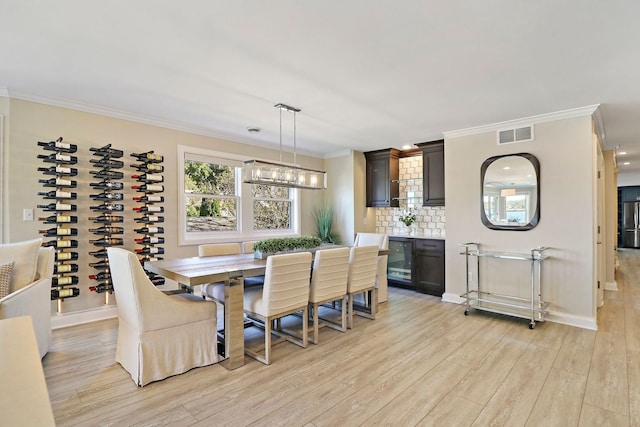 dining room featuring wine cooler, light hardwood / wood-style flooring, ornamental molding, and a notable chandelier