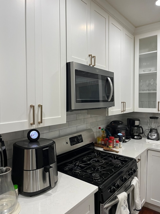 kitchen with light stone countertops, stainless steel appliances, backsplash, and white cabinetry