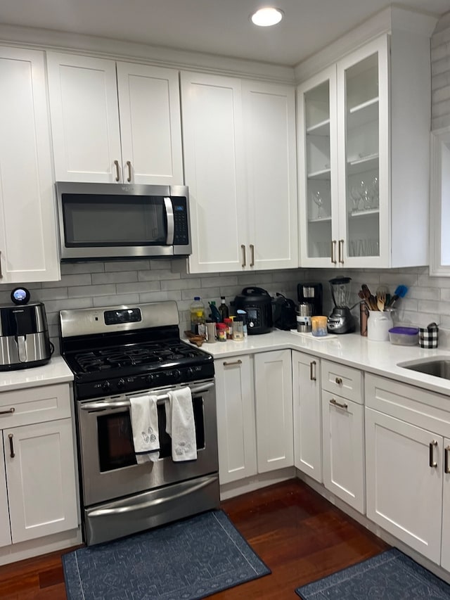 kitchen with stainless steel appliances, backsplash, white cabinets, and dark wood-type flooring