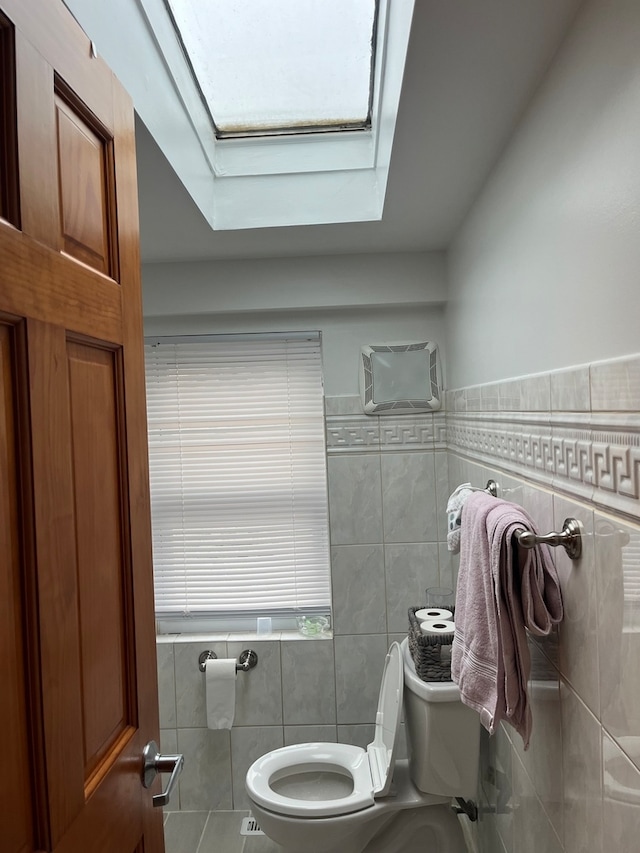 bathroom featuring a skylight, a wall unit AC, tile walls, and toilet