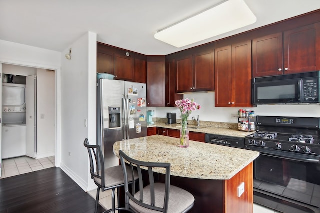 kitchen featuring black appliances, light stone countertops, a center island, a breakfast bar area, and light hardwood / wood-style flooring