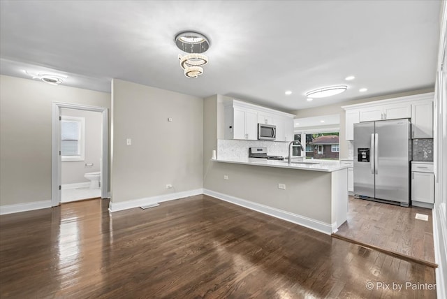 kitchen featuring sink, dark hardwood / wood-style flooring, kitchen peninsula, stainless steel appliances, and white cabinets