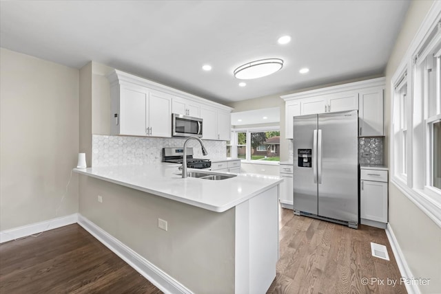 kitchen with kitchen peninsula, white cabinets, appliances with stainless steel finishes, wood-type flooring, and sink