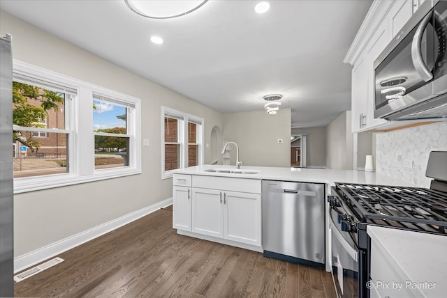 kitchen with wood-type flooring, appliances with stainless steel finishes, sink, kitchen peninsula, and white cabinets