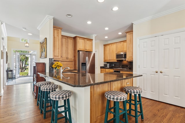 kitchen featuring backsplash, light hardwood / wood-style floors, stainless steel appliances, dark stone countertops, and a breakfast bar