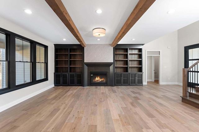 unfurnished living room featuring a fireplace, beam ceiling, and light hardwood / wood-style flooring