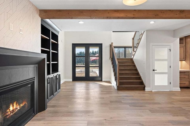 foyer entrance with light wood-type flooring, beam ceiling, a tile fireplace, and french doors