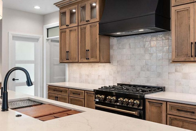 kitchen featuring sink, backsplash, custom range hood, and gas stove