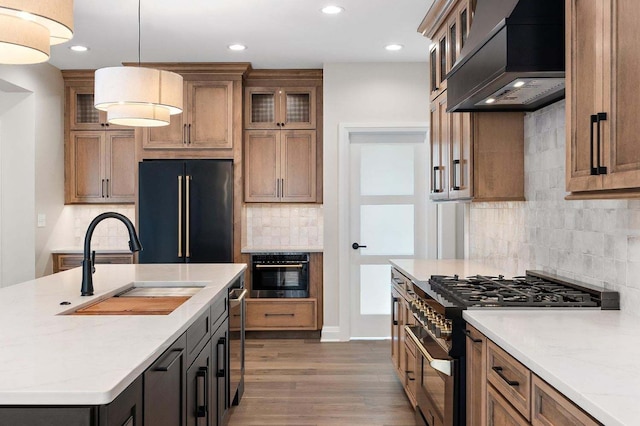 kitchen featuring an island with sink, dark hardwood / wood-style floors, premium range hood, premium appliances, and pendant lighting