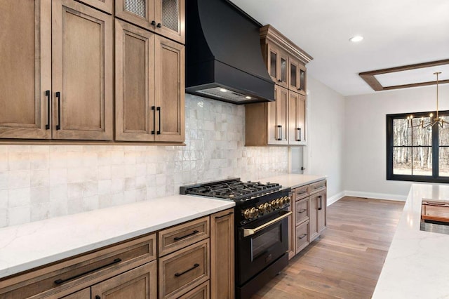 kitchen with light wood-type flooring, light stone countertops, custom range hood, hanging light fixtures, and range with gas cooktop