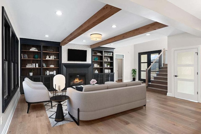 living room with built in features, beam ceiling, and light wood-type flooring