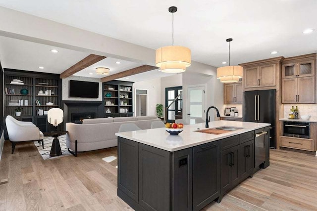 kitchen featuring a kitchen island with sink, sink, light hardwood / wood-style floors, beam ceiling, and decorative light fixtures