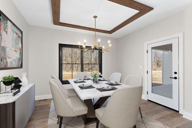 dining space featuring a raised ceiling, wood-type flooring, and an inviting chandelier