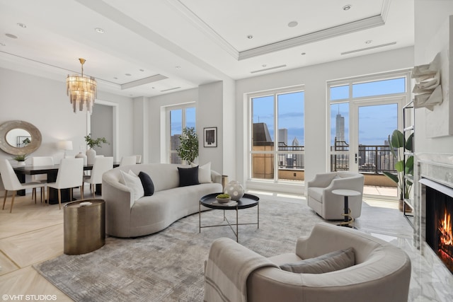 living room with ornamental molding, a tray ceiling, a high end fireplace, and an inviting chandelier