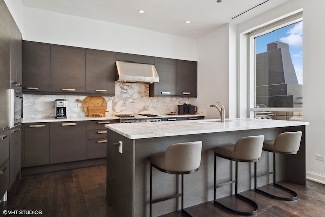 kitchen featuring sink, a kitchen bar, dark hardwood / wood-style flooring, wall chimney exhaust hood, and a kitchen island with sink