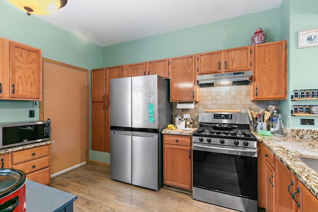 kitchen featuring light stone counters, appliances with stainless steel finishes, light wood-type flooring, and decorative backsplash