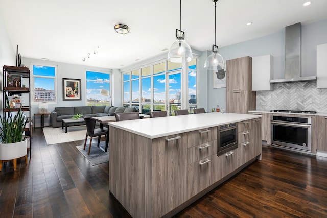 kitchen with tasteful backsplash, wall chimney range hood, appliances with stainless steel finishes, a center island, and dark hardwood / wood-style floors