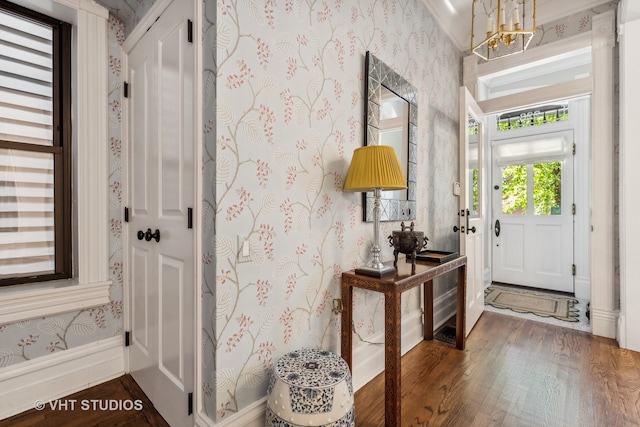 foyer with ornamental molding, dark wood-type flooring, and an inviting chandelier