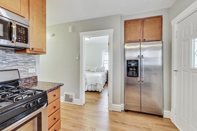 kitchen featuring stainless steel appliances, dark stone counters, light hardwood / wood-style floors, and a wealth of natural light