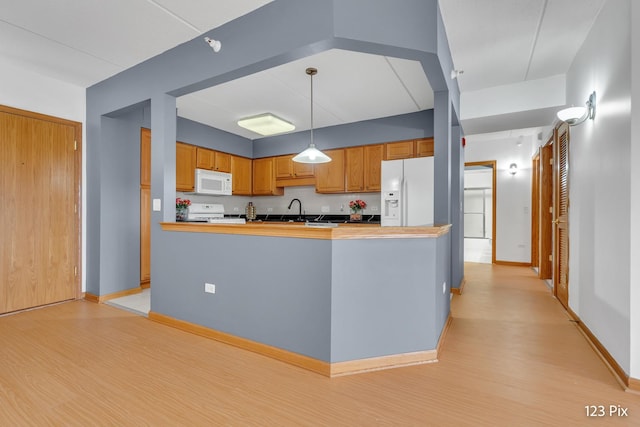 kitchen featuring kitchen peninsula, light wood-type flooring, white appliances, sink, and decorative light fixtures