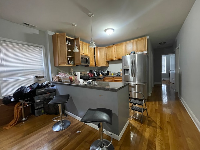 kitchen featuring a breakfast bar area, kitchen peninsula, stainless steel appliances, pendant lighting, and dark hardwood / wood-style flooring