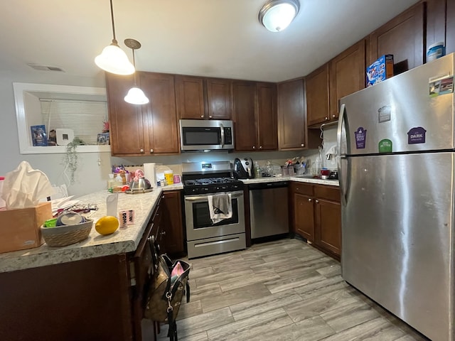 kitchen featuring sink, appliances with stainless steel finishes, hanging light fixtures, and light hardwood / wood-style flooring