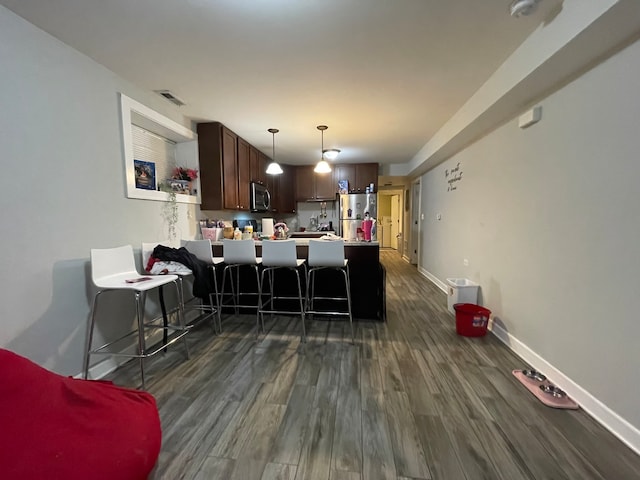 kitchen featuring kitchen peninsula, a breakfast bar area, dark wood-type flooring, pendant lighting, and stainless steel appliances