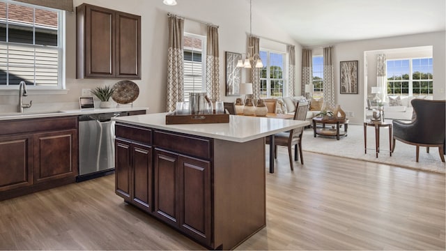 kitchen featuring a kitchen island, stainless steel dishwasher, sink, hanging light fixtures, and light hardwood / wood-style flooring