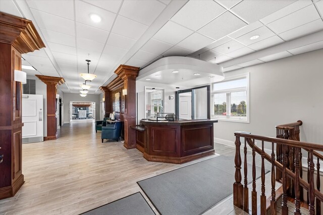 interior space with ornate columns, a paneled ceiling, a center island with sink, and light hardwood / wood-style flooring