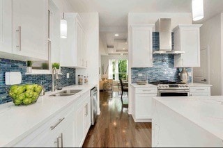 kitchen with stainless steel appliances, white cabinets, sink, wall chimney range hood, and decorative light fixtures