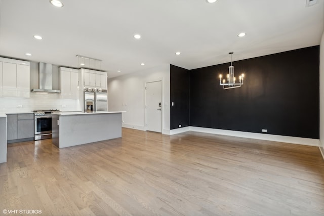 kitchen with white cabinets, decorative light fixtures, wall chimney exhaust hood, light hardwood / wood-style flooring, and appliances with stainless steel finishes