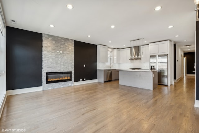 interior space with wall chimney exhaust hood, pendant lighting, stainless steel appliances, white cabinets, and a center island