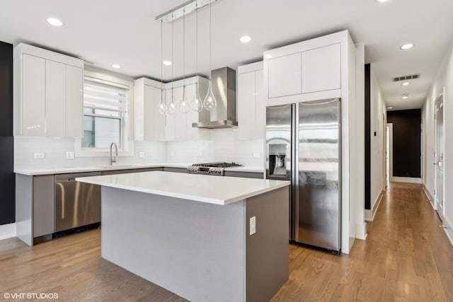 kitchen with pendant lighting, white cabinets, a kitchen island, wall chimney range hood, and appliances with stainless steel finishes