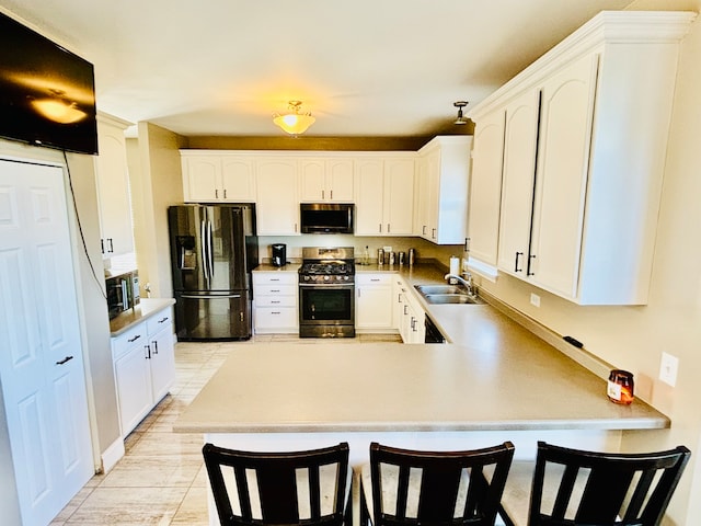 kitchen with appliances with stainless steel finishes, sink, kitchen peninsula, white cabinets, and a breakfast bar