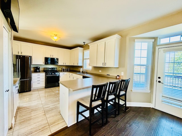 kitchen featuring a breakfast bar area, kitchen peninsula, black appliances, light wood-type flooring, and white cabinetry