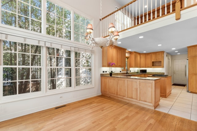 kitchen featuring kitchen peninsula, dark stone counters, an inviting chandelier, and light hardwood / wood-style flooring