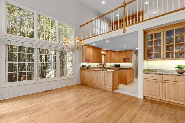 kitchen featuring a high ceiling, light stone countertops, an inviting chandelier, and light hardwood / wood-style floors