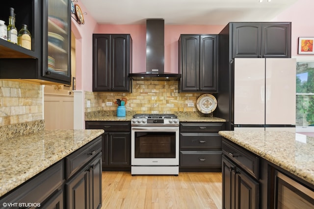 kitchen featuring light stone counters, white appliances, tasteful backsplash, wall chimney exhaust hood, and light hardwood / wood-style floors