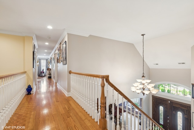 corridor with light hardwood / wood-style floors, vaulted ceiling, a chandelier, and ornamental molding