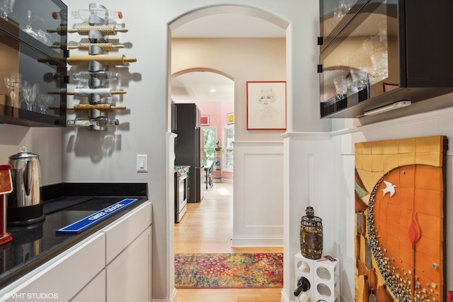 bar featuring stainless steel range with gas stovetop, light wood-type flooring, and white cabinetry