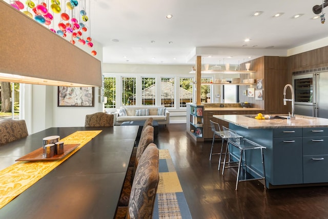 kitchen featuring an island with sink, a breakfast bar area, dark hardwood / wood-style flooring, built in refrigerator, and light stone countertops