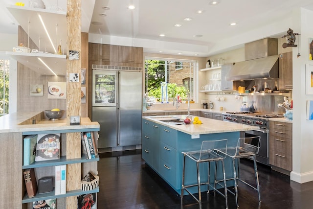 kitchen with a kitchen island, premium appliances, decorative backsplash, dark wood-type flooring, and wall chimney range hood