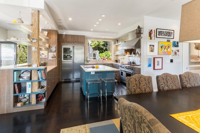 kitchen with dark hardwood / wood-style flooring, a kitchen breakfast bar, high end appliances, a center island, and wall chimney range hood