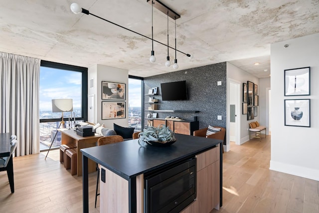 kitchen featuring hanging light fixtures, a kitchen island, light hardwood / wood-style floors, a kitchen bar, and black microwave