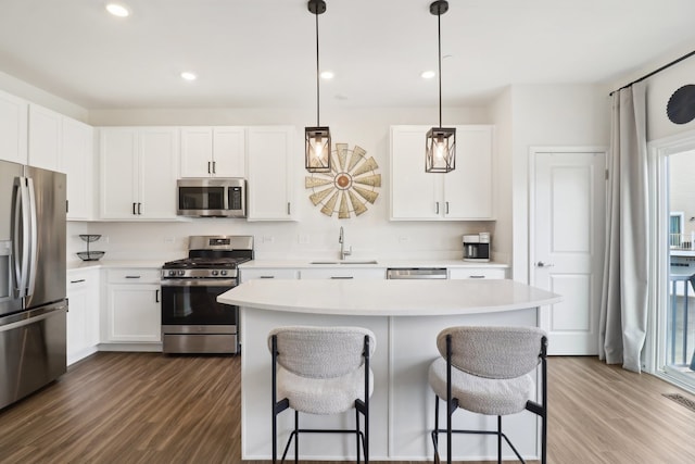 kitchen with a kitchen island, stainless steel appliances, wood-type flooring, pendant lighting, and white cabinets