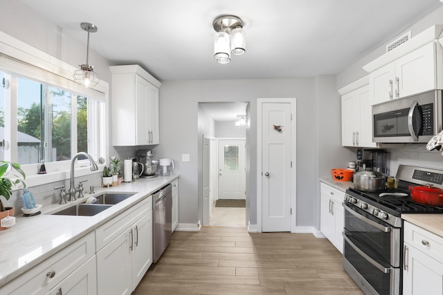 kitchen featuring pendant lighting, sink, white cabinetry, stainless steel appliances, and light wood-type flooring