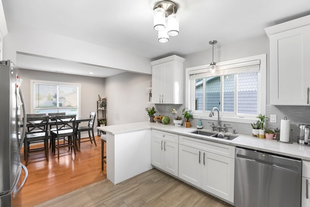 kitchen featuring light hardwood / wood-style floors, sink, kitchen peninsula, white cabinets, and appliances with stainless steel finishes